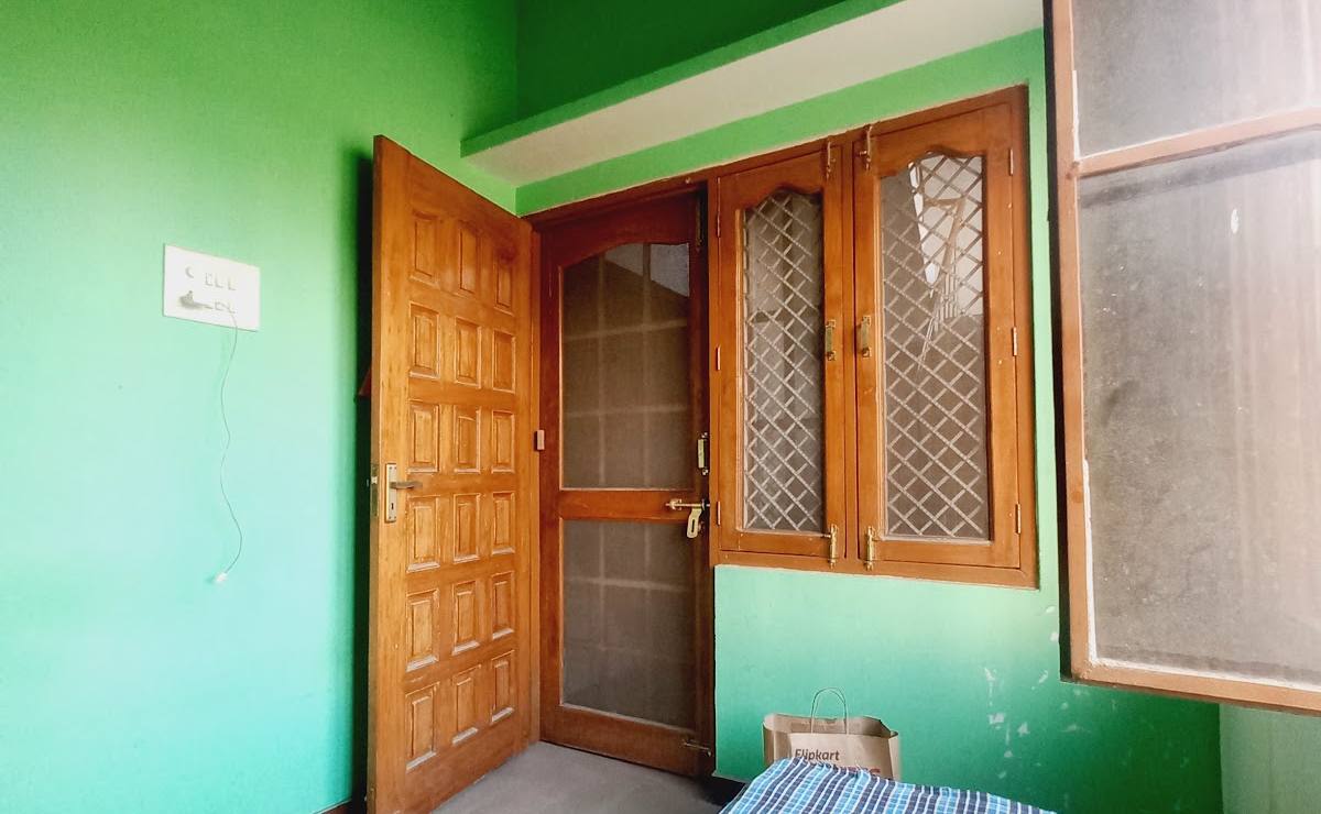 A green room with a wooden door, a big window and a bed