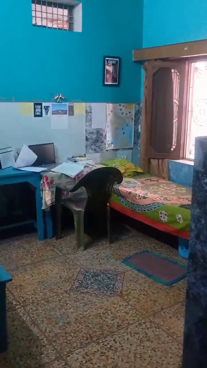 A room with a study desk, a laptop, a bed, and notes and maps on the wall