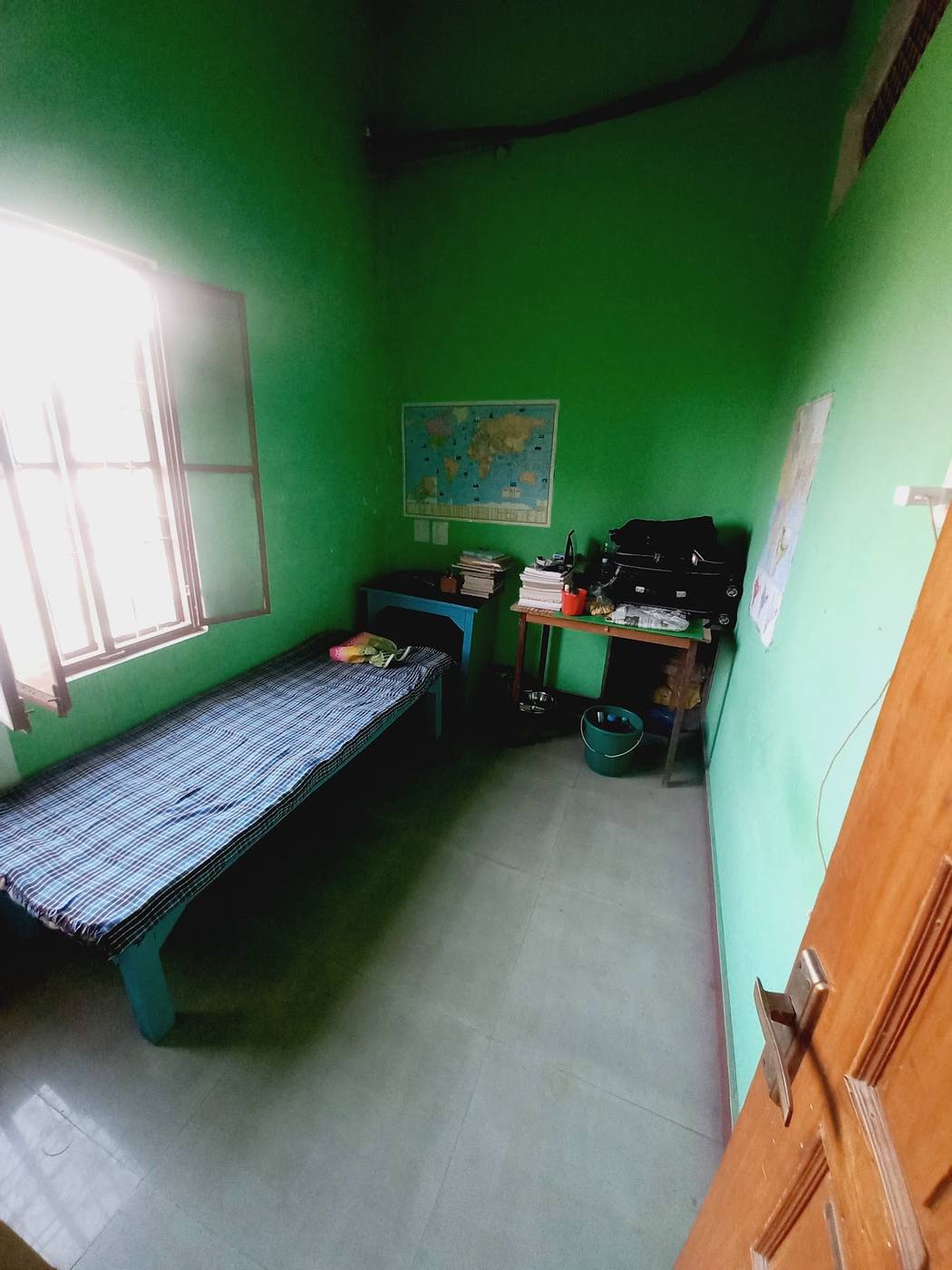 A single room with a bed, two small study tables and a world map