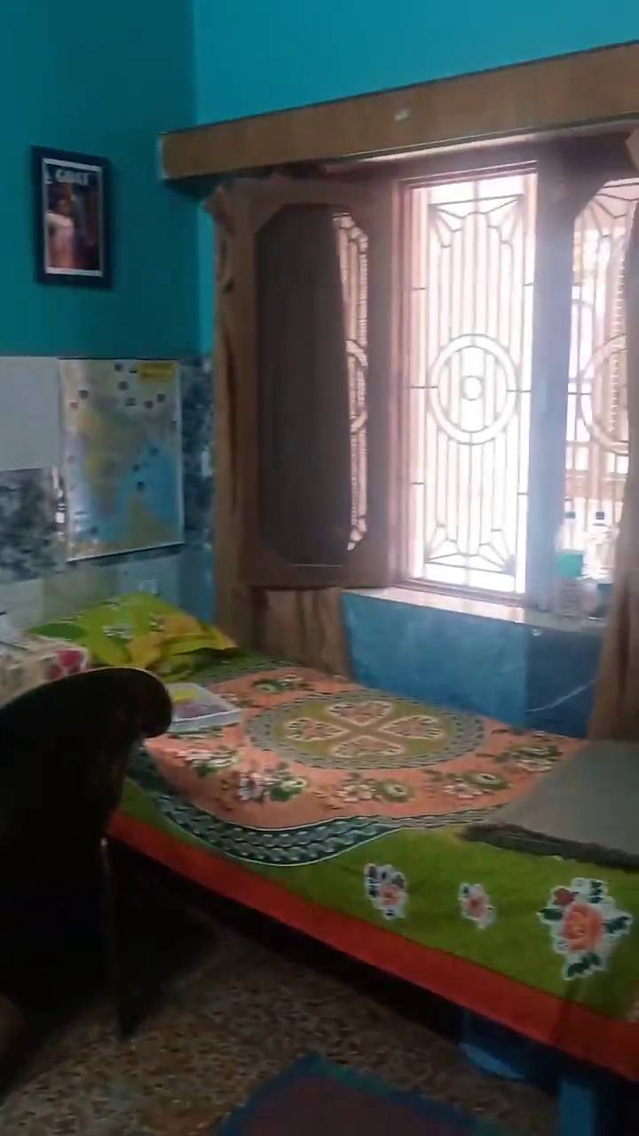 A bed with a floral sheet beside a grilled window, in a turquoise room
